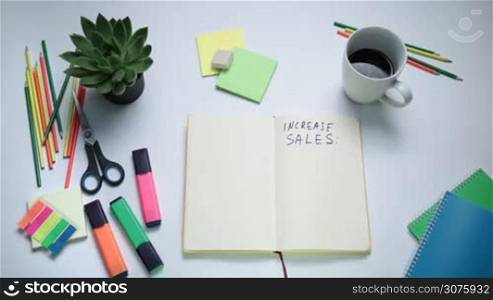 Top view of human hand writing words on notebook with board marker. Woman writing steps to increase sales on white note pad