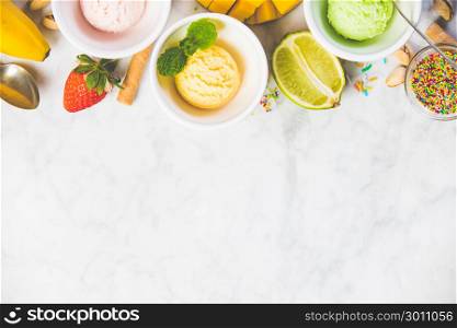 Top view of ice cream in white bowls and fresh ingredients on white marble background. Pink (strawberry), yellow (mango or banana) and green (lime, green tea or pistachio).
