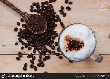 Top view of iced coffee froth in coffee mug with coffee beens and coffee powders on a wooden floor.