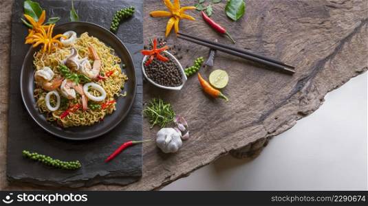 Top view of instant noodles with stir fried spicy seafood and various spices on wooden table top in vintage tone style, junk food and Asian meal concept