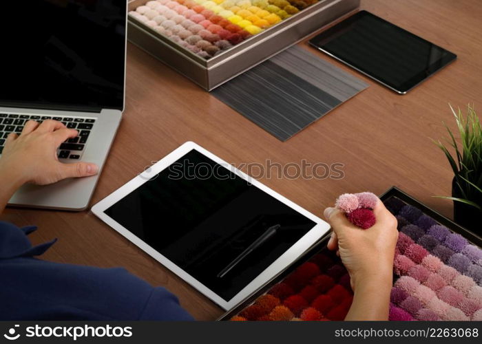 top view of Interior designer hand chosing carpet sample with blank new modern computer laptop and pro digital tablet with material board and digital design diagram layer on wooden desk as concept