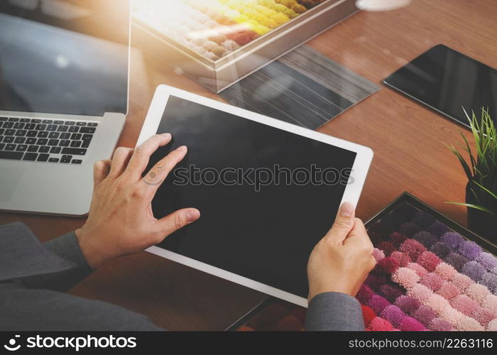 top view of Interior designer hand chosing carpet sample with blank new modern computer laptop and pro digital tablet with material board and digital design diagram layer on wooden desk as concept