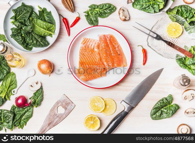 Top view of kitchen table with salmon , spinach leaves , kitchen knife and pan, cooking preparation on white wooden background , top view