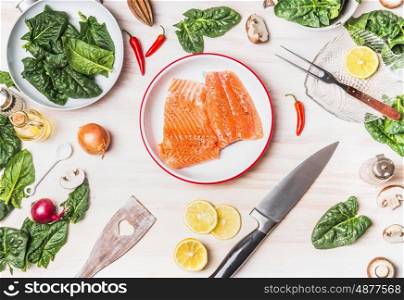 Top view of kitchen table with salmon , spinach leaves , kitchen knife and pan, cooking preparation on white wooden background , top view