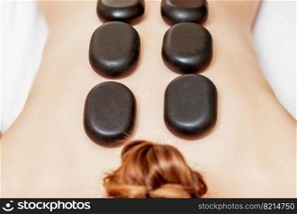 Top view of large new oval black hot stones for back massage lying on female back in spa salon. Black hot stones lying on female back