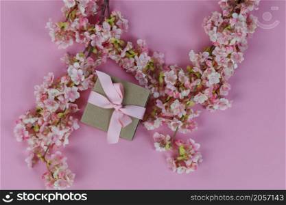 Top view of light cherry blossom flowers and a giftbox on a pink background for Mothers Day or Easter holiday concept