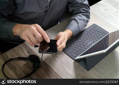 top view of man hand using VOIP headset with digital tablet computer docking keyboard,smart phone,concept communication, it support, call center and customer service help desk on wooden table