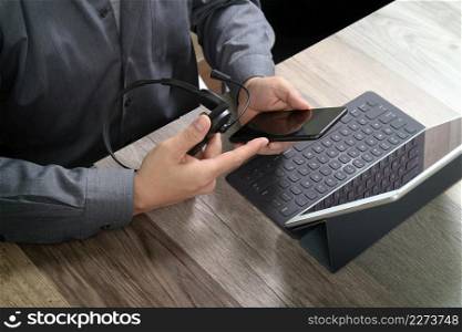 top view of man hand using VOIP headset with digital tablet computer docking keyboard,smart phone,concept communication, it support, call center and customer service help desk on wooden table