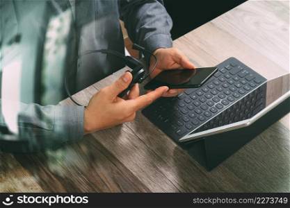 top view of man hand using VOIP headset with digital tablet computer docking keyboard,smart phone,concept communication, it support, call center and customer service help desk on wooden table,filter