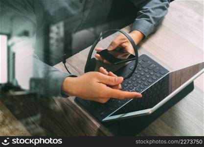 top view of man hand using VOIP headset with digital tablet computer docking keyboard,smart phone,concept communication, it support, call center and customer service help desk on wooden table,filter