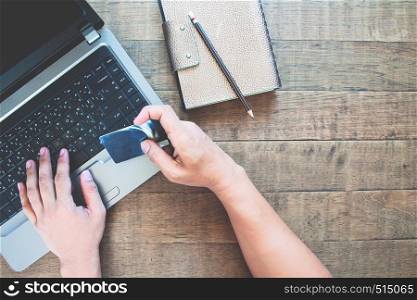 Top view of man's hands holding credit card and using smart phone on wooden table. Online shopping concept