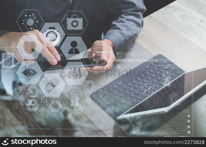 top view of medical doctor hand working with smart phone,digital tablet computer,stethoscope eyeglass,on wooden desk,virtual graphic interface icons screen