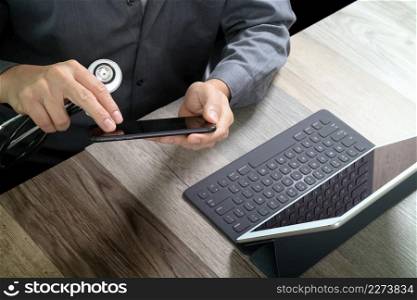 top view of medical doctor hand working with smart phone,digital tablet computer,stethoscope eyeglass,on wooden desk