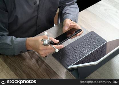 top view of medical doctor working with mobile phone and digital tablet computer and stethoscope on wooden desk