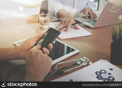 top view of Medicine doctor hand working with modern computer and digital pro tablet and smart phone with digital medical diagram with his team on wooden desk as medical concept