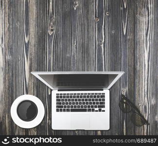 Top view of modern working business office desk - notebook or laptop, coffee and glasses on wood table texture background.