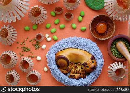 Top view of moon cake with mother pig and piglets shape, baking materials, paper lanterns, traditional baked pastry for mid autumn season on orange background