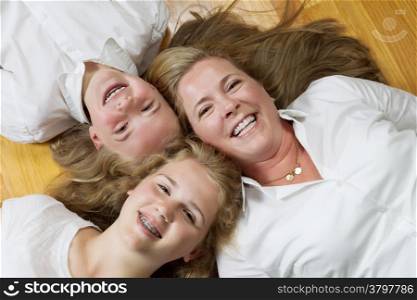 Top view of mother and her daughters lying on oak floor while looking forward