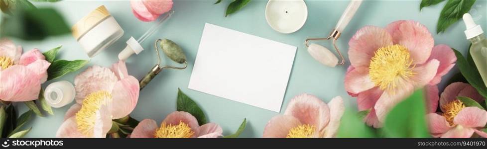 Top view of natural cosmetics and pink peonies on pastel blue background with white card for invitation, logo or design flat lay copy space