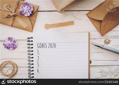 Top view of New Year Goals 2020 list empty note pad and christmas card on wooden table with xmas decoration.
