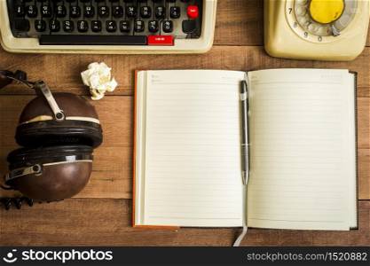 Top view of notebook on the wood table , typewriter, old telephone and earphone