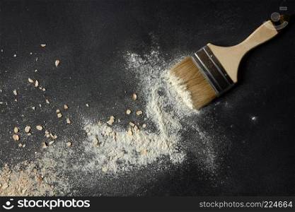 Top view of oat flakes and flour with brush over black background. Brush with oat flakes and flour