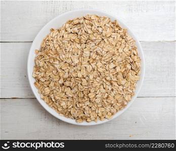 Top view of oat flakes in a bowl on wooden background