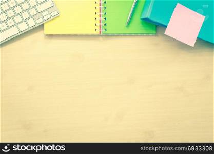 Top view of office place with blank desk space. Color paper book, white keyboard, pen, binder and sticky note on top side. Mockup background template, sepia photograph, vintage and retro styles.