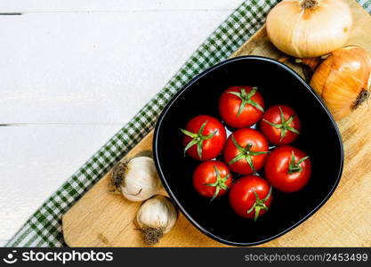 Top view of onions, garlic and fresh ripe cherry tomatoes on a rustic white wooden table. Ingredients and food concept