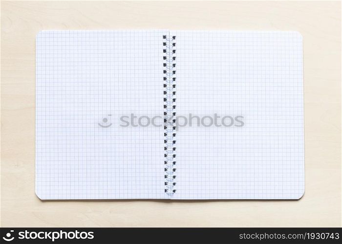 top view of open blank spiral notebook with squared pages on light brown wooden board