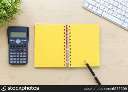 Top view of open book with yellow blank pages, calculator, modern keyboard, plants and black premium pen on workspace table background. Business management concept, minimal style.