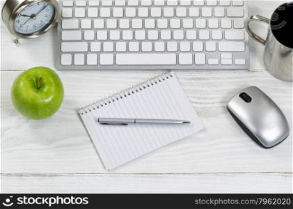 Top view of organized white wooden desktop with office work objects. Layout in horizontal format with mostly silver objects.