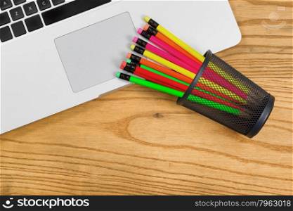 Top view of partial computer laptop with colorful pencils in cup on desktop.