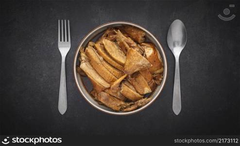 top view of Ped Pa Lo, tasty brown Chinese stewed duck in bowl with spoon and fork on dark gray, grey, black tone texture background