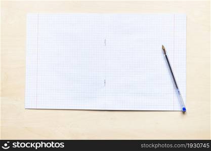 top view of pen and blank open school notebook with squared sheets with margins on light brown wooden board
