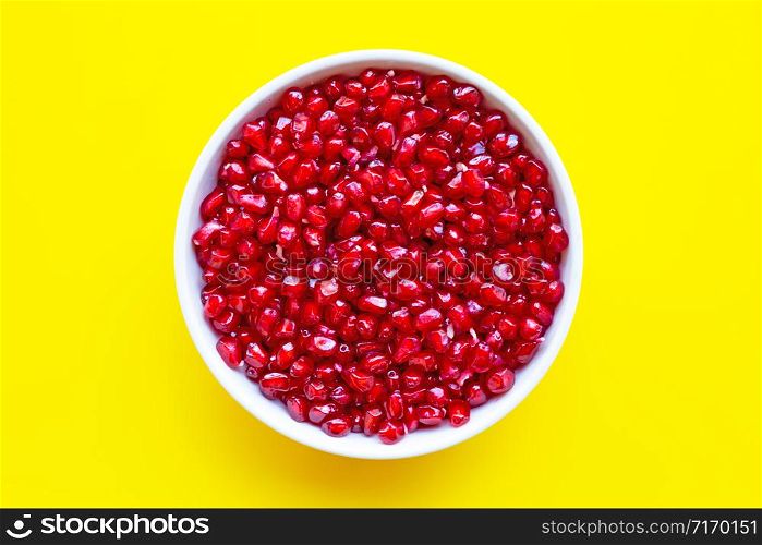 Top view of pomegranate seed in white bowl on yellow background.