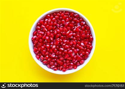 Top view of pomegranate seed in white bowl on yellow background.
