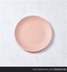 Top view of porcelain plate handmade. Ceramic glazed plate is empty on a gray background with copy space. Can be used for display or montage your products.. Traditional decorative handcrafted clay dish, covered with glazed on a gray concrete background. Flat lay