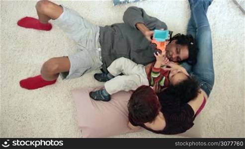 Top view of positive interracial family bonding to each other and cuddling while lying on the floor. Overhead. Happy african american father and caucasian mother playing with their mixed race toddler son. Happy family together. Slow motion.