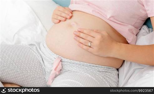 Top view of pregnant woman wearing pajamas holfding and touching her big tummy. Concept of parenting and happy expectation of future baby. Top view of pregnant woman wearing pajamas holfding and touching her big tummy. Concept of parenting and happy expectation of future baby.