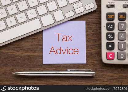 "Top view of purple notepad with words " Tax Advice " putting on workspace with keyboard, calculator and stainless steel pen on wood table"