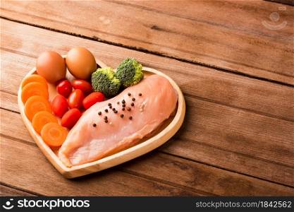 Top view of Raw chicken breasts fillets no boneless with spices rosemary, carrot, and eggs in heart plate wood on wooden background, Healthy food day concept