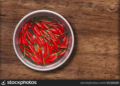 Top view of red chilli pepper in water on bowl of steel on wooden background,copy space