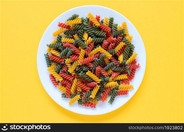 Top view of red green and yellow dry raw fusilli pasta on a plate with yellow background.. Red green and yellow dry raw fusilli pasta on a plate with yellow background.