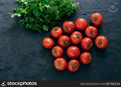 Top view of red ripe fresh tomatoes with green parsley on dark background. Vitamins and nutrition concept. Copy space. Raw food
