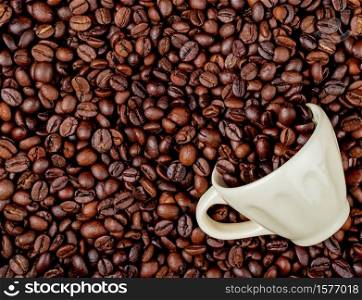 top view of roasted coffee beans scattered from a ceramic cup on coffee beans background