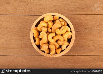 Top view of salted cashew nuts in wooden bowl on wood background