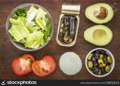 top view of sardine salad ingredients - romaine lettuce, tomato, onion, olives, avocado and canned sardines
