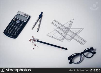 Top view of school supplies on clean white desktop background with calculator, paper compass, rulers, glasses, pencil and sharpener with wooden shavings - Concept of college student, university education, learning or high school.. Top view of school supplies on clean white desktop background with calculator, paper compass, rulers, glasses, pencil and sharpener with wooden shavings - Concept of college student, university education, learning or high school