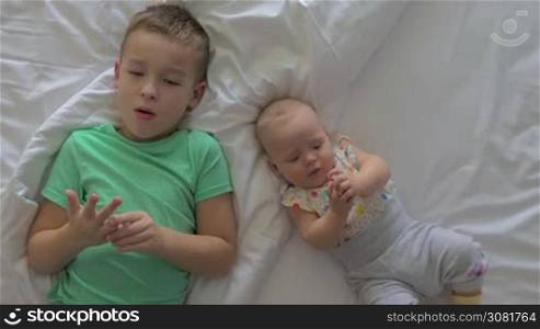 Top view of seven years old boy with junior baby sister of six months lying on bed together